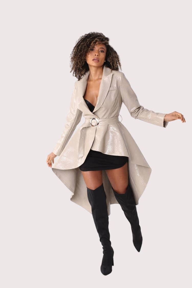 Woman wearing a long beige coat over a black dress with knee-high black boots on a white background