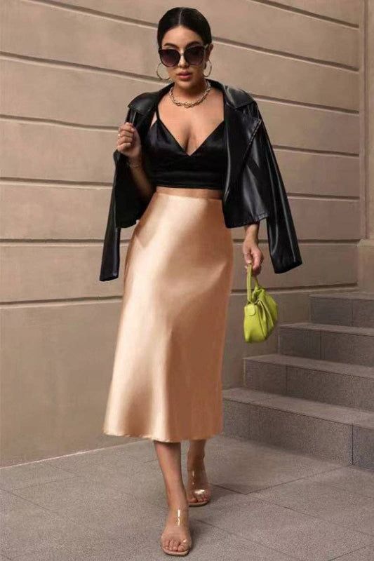 Woman in black leather jacket, black top, and gold skirt standing on steps.
