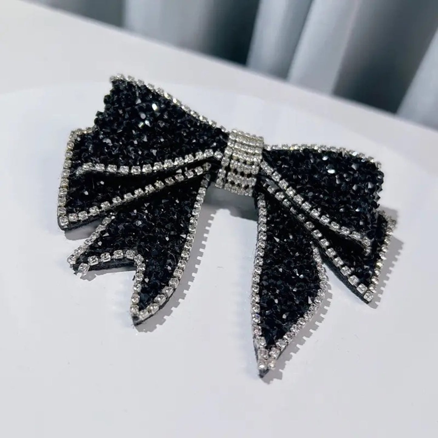 Black bow-shaped earrings with rhinestone details on a white surface.