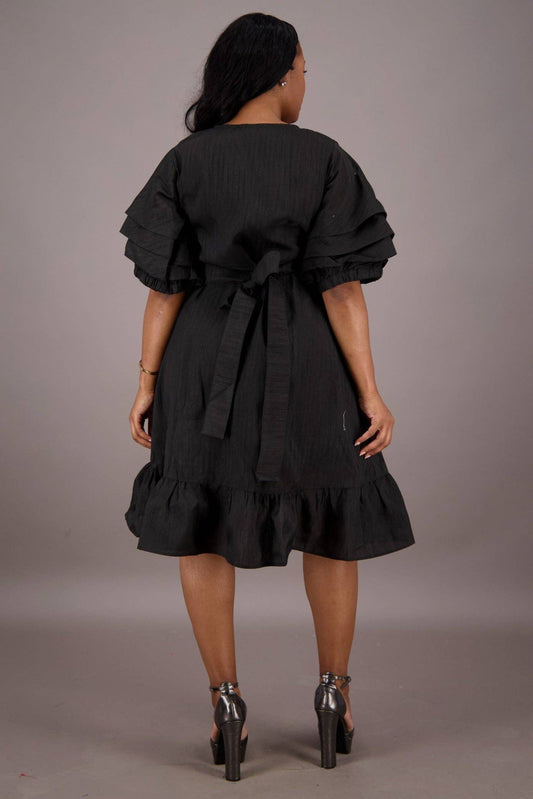 A model wearing a black Empress Ruffle Wrap Dress with a V-neckline, embroidery details, and voluminous sleeves. The dress features a cascading ruffle trim and a wrap silhouette.