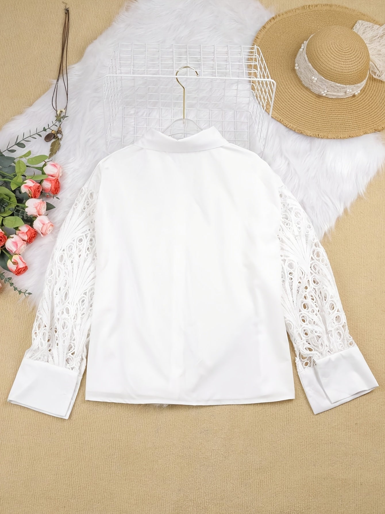 White lace top on a beige surface with a straw hat and flowers.