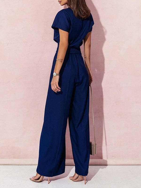 Woman wearing a navy blue jumpsuit against a pink wall