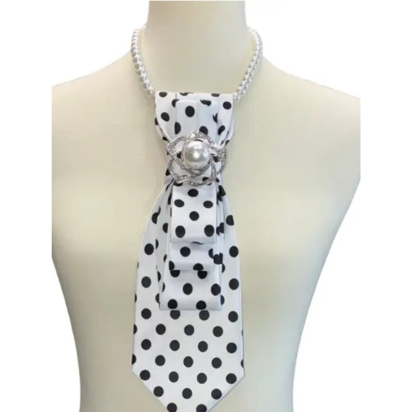 White mannequin wearing a black and white polka dot scarf with a pearl brooch on a white background