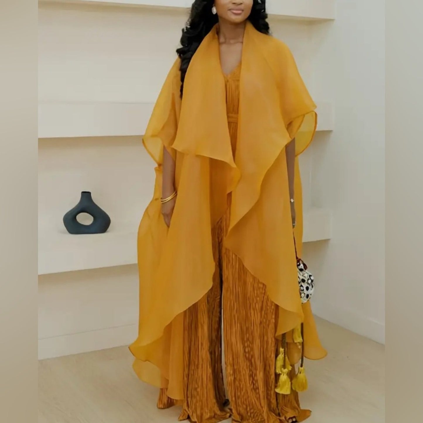 Woman wearing a mustard yellow outfit with a flowing top and patterned pants in an indoor setting.