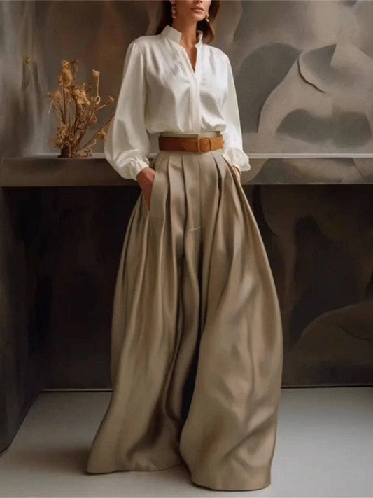 Person wearing a white blouse and beige wide-leg pants with a brown belt, standing against a neutral background.