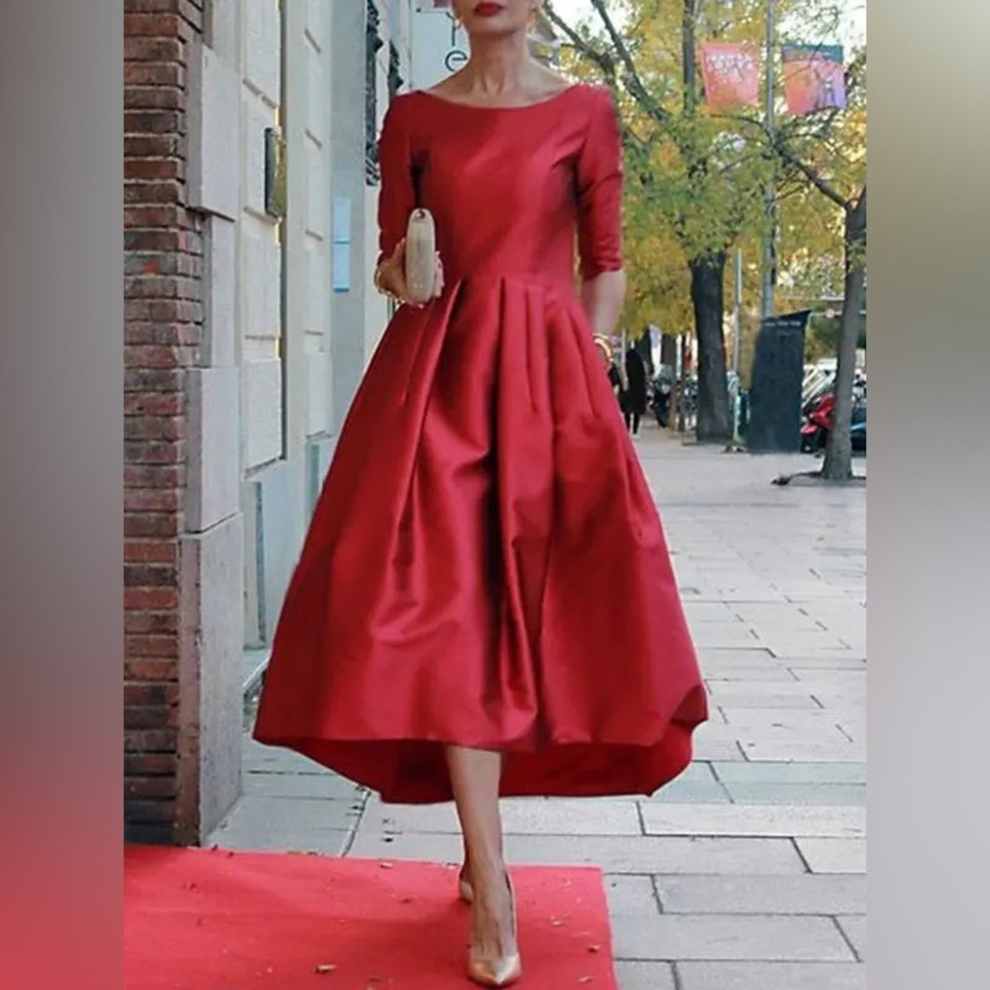 Woman in a red dress standing on a red carpet in an urban setting