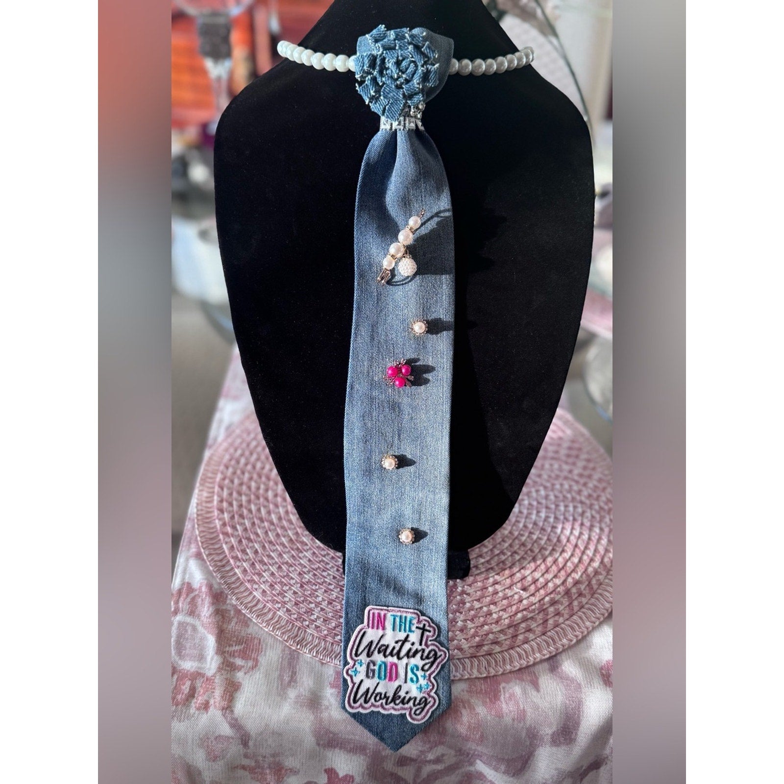 Decorative denim tie with buttons and a floral design on a black mannequin.