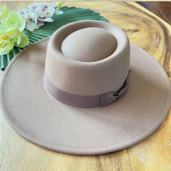 Beige wide-brimmed hat with a ribbon on a wooden surface with flowers in the background