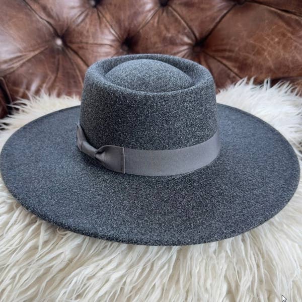 Gray fedora hat with a ribbon on a fluffy white surface with a brown leather couch in the background.