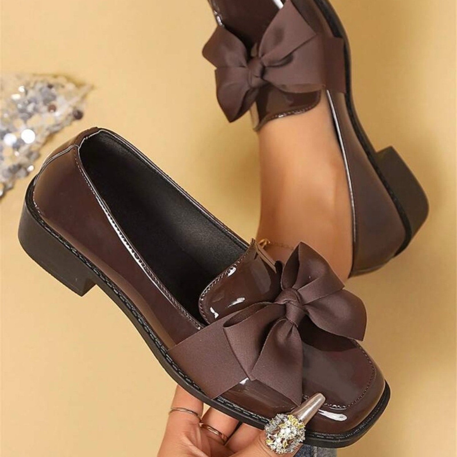 Brown shoes with large bows held by a hand on a beige background