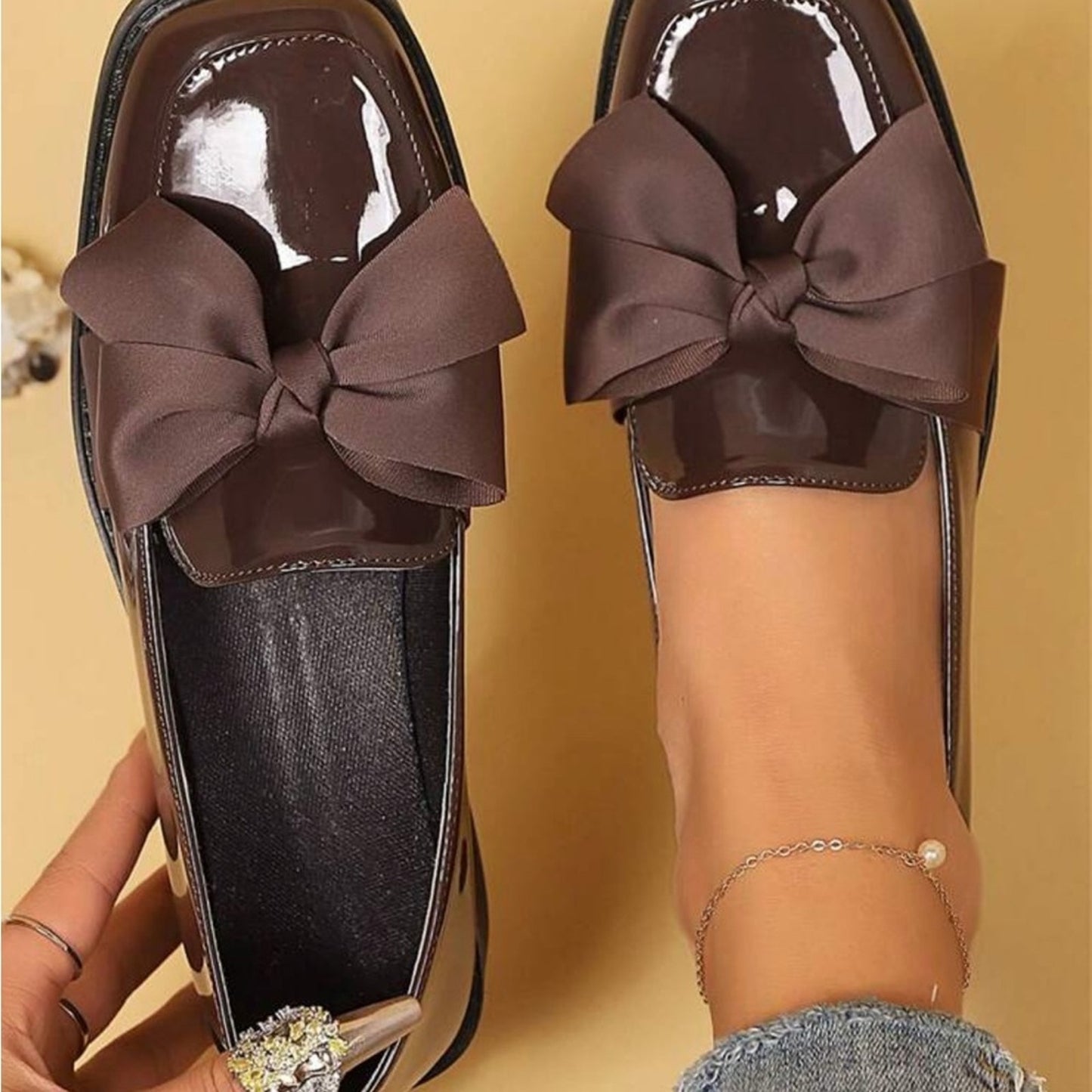 Brown shoes with large bows worn by a person on a yellow background