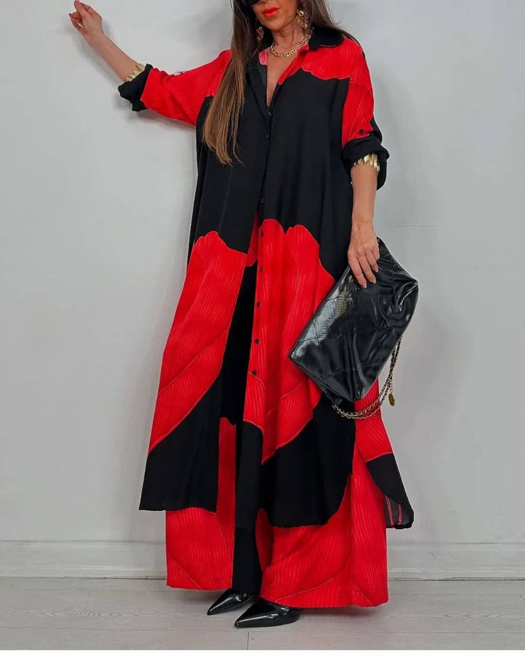 Woman wearing a black and red dress holding a black clutch against a gray background