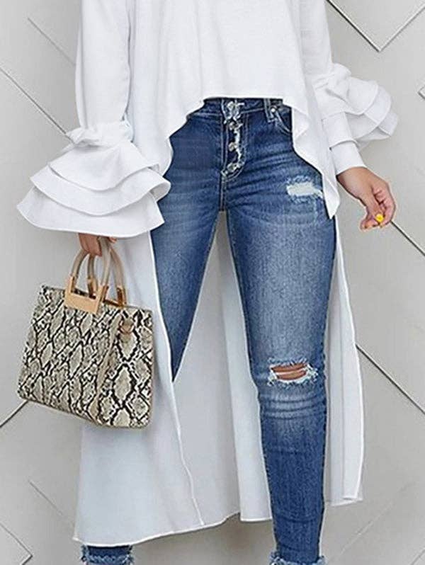Person wearing a white blouse, blue jeans, and holding a snake print handbag on a light background