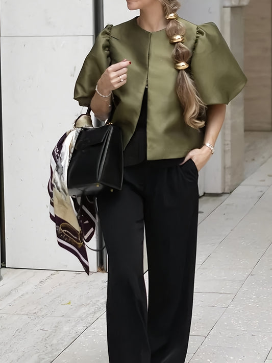 Woman wearing a green top and black pants with a black handbag, standing on a sidewalk.