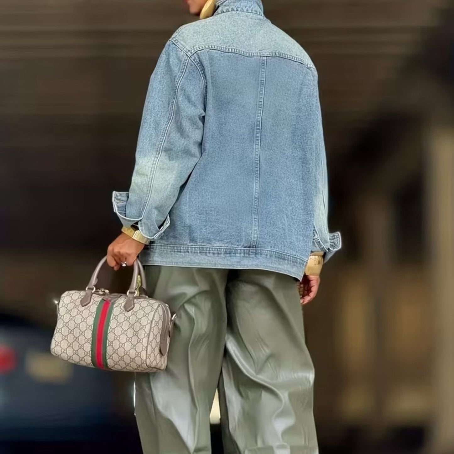 Person wearing a denim jacket and holding a Gucci handbag with a blurred background