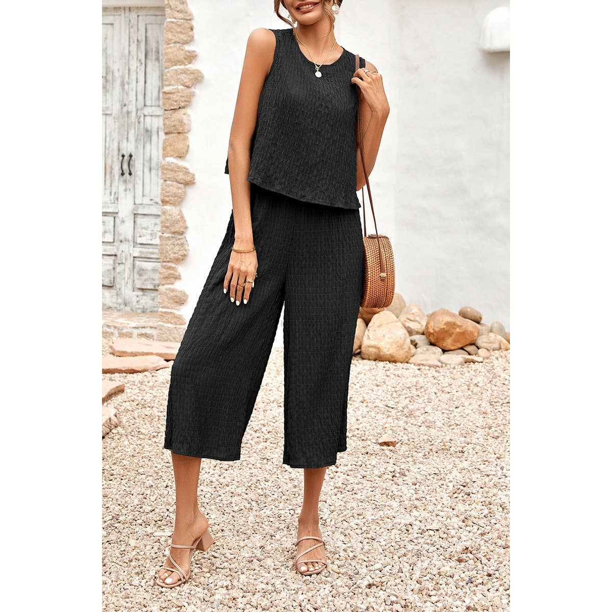 Woman wearing a black sleeveless top and wide-leg pants standing outdoors.