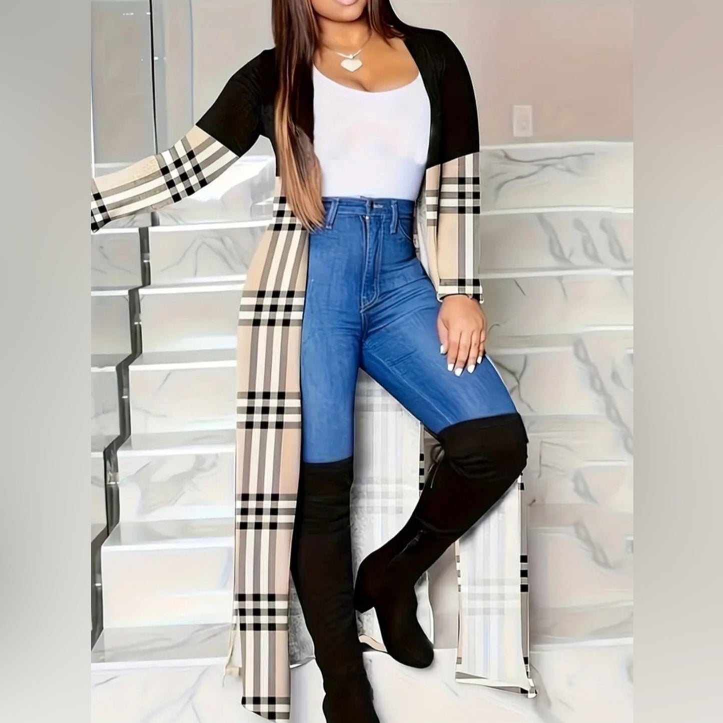 Woman wearing a checkered long cardigan, white top, blue jeans, and black knee-high boots on a marble staircase.