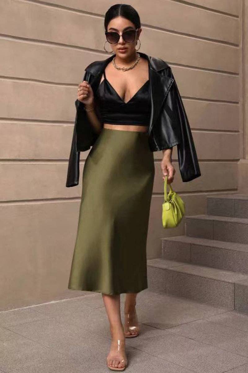 Woman in black leather jacket and green skirt standing on steps with a beige wall background
