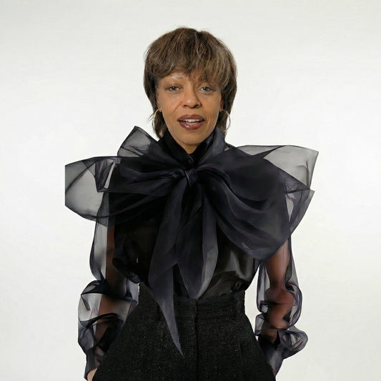 Person wearing a black sheer blouse with a large bow on a white background