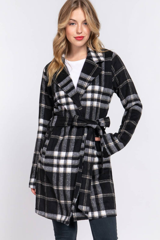 A female model wearing a black  long sleeve belted plaid woven jacket with a checkered pattern.