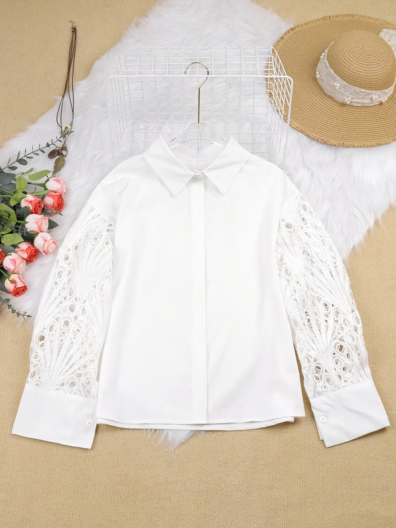 White blouse with lace sleeves on a beige surface with a hat and flowers.