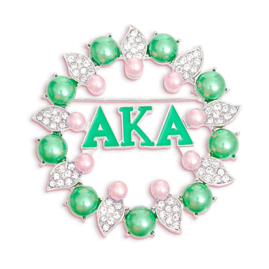 Decorative brooch with 'AKA' letters surrounded by green and pink beads on a white background