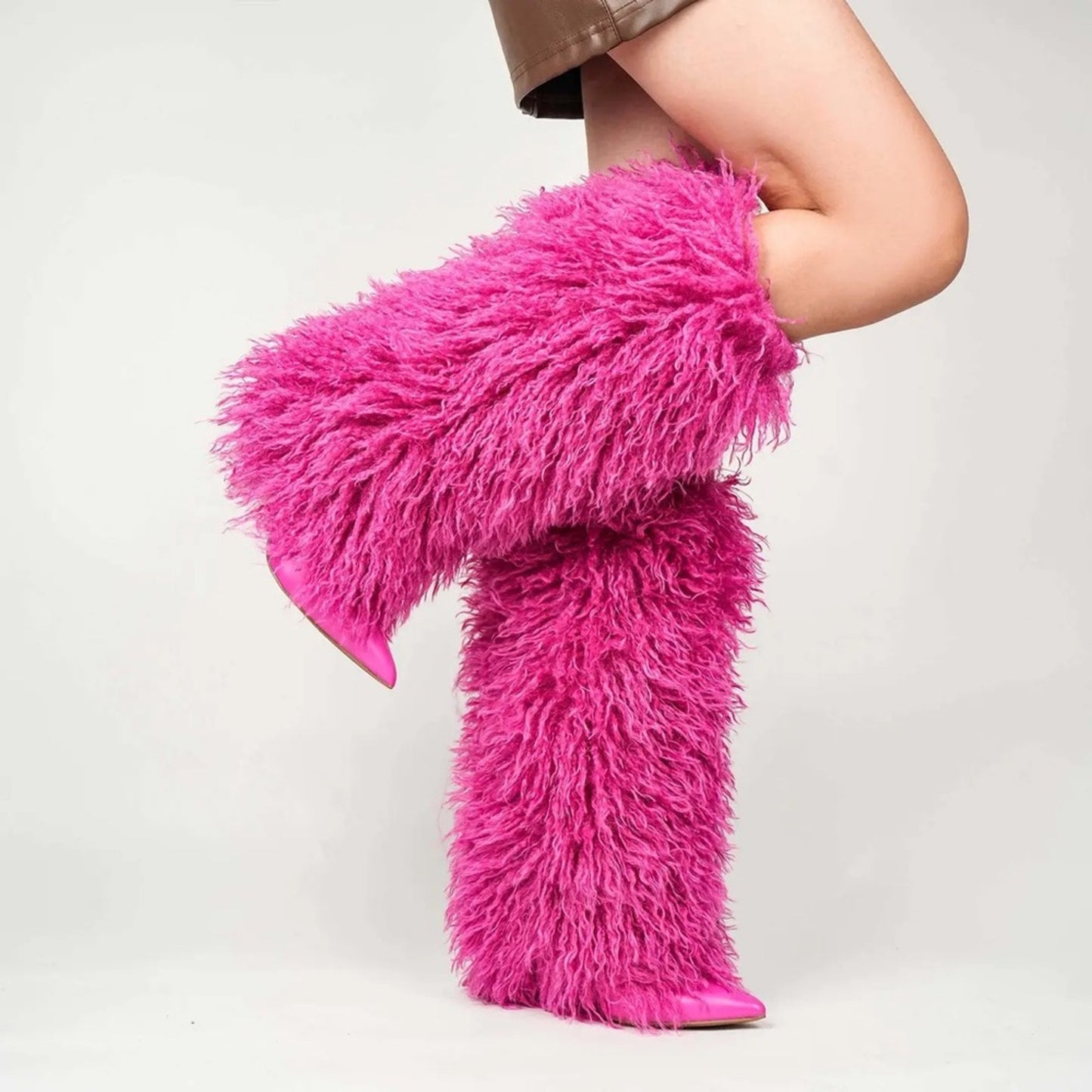 Pink furry leg warmers worn by a person on a plain background
