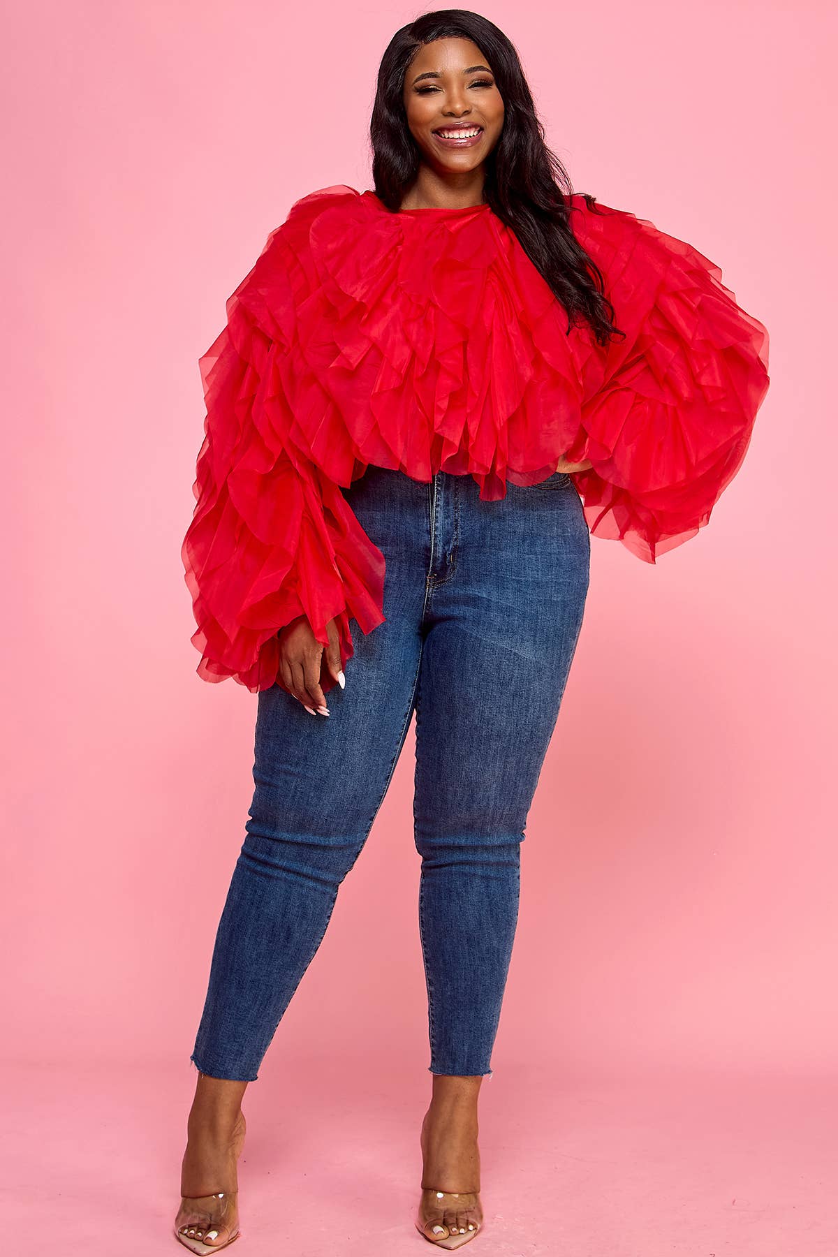Woman wearing a red ruffled top and blue jeans on a pink background