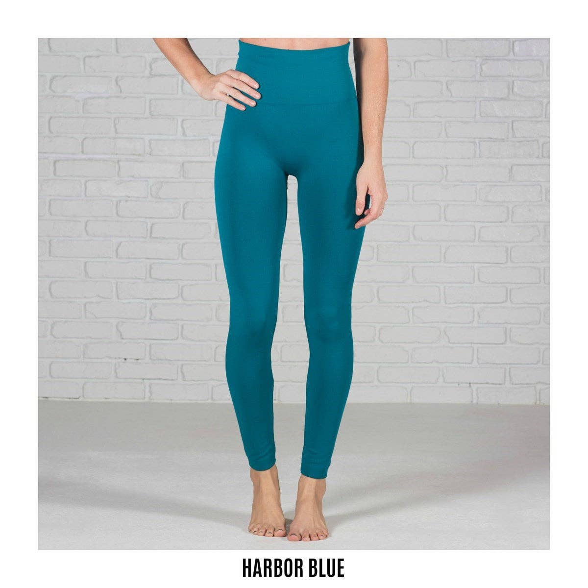 Teal leggings worn by a person against a light gray brick wall.