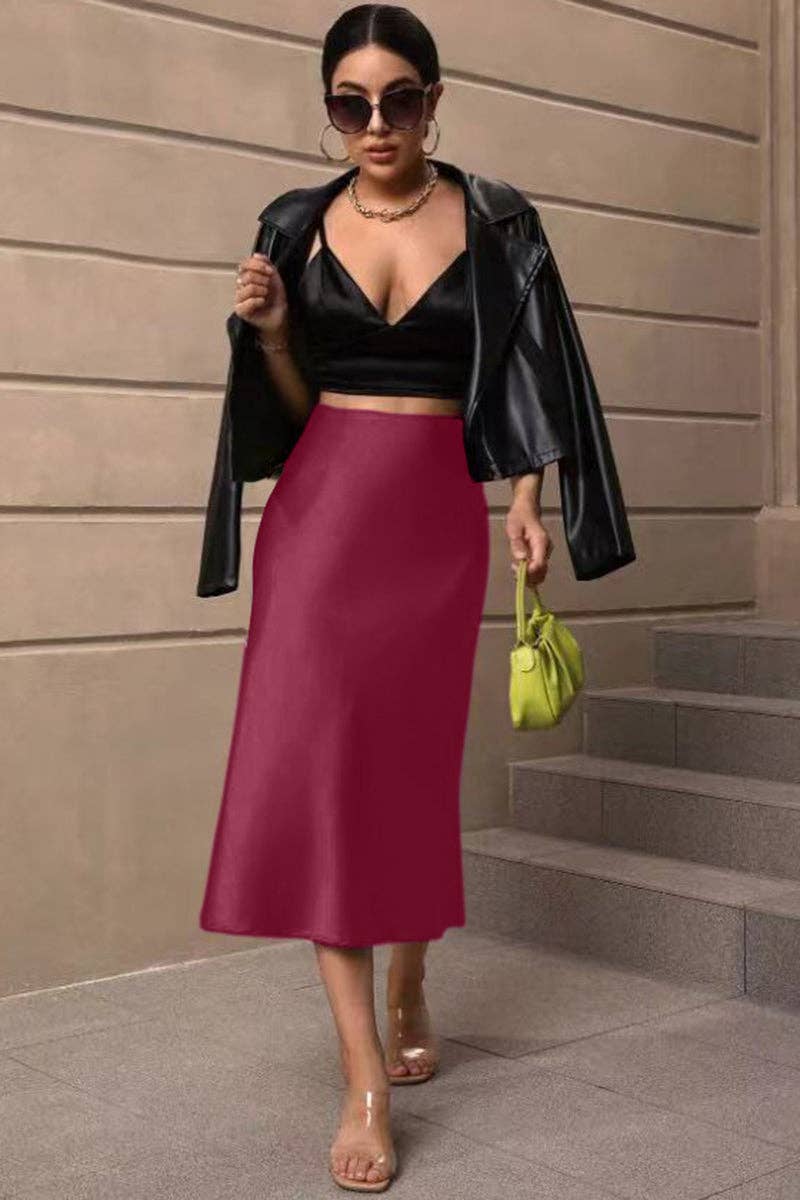 Woman in black top and red skirt with green handbag against a beige wall.