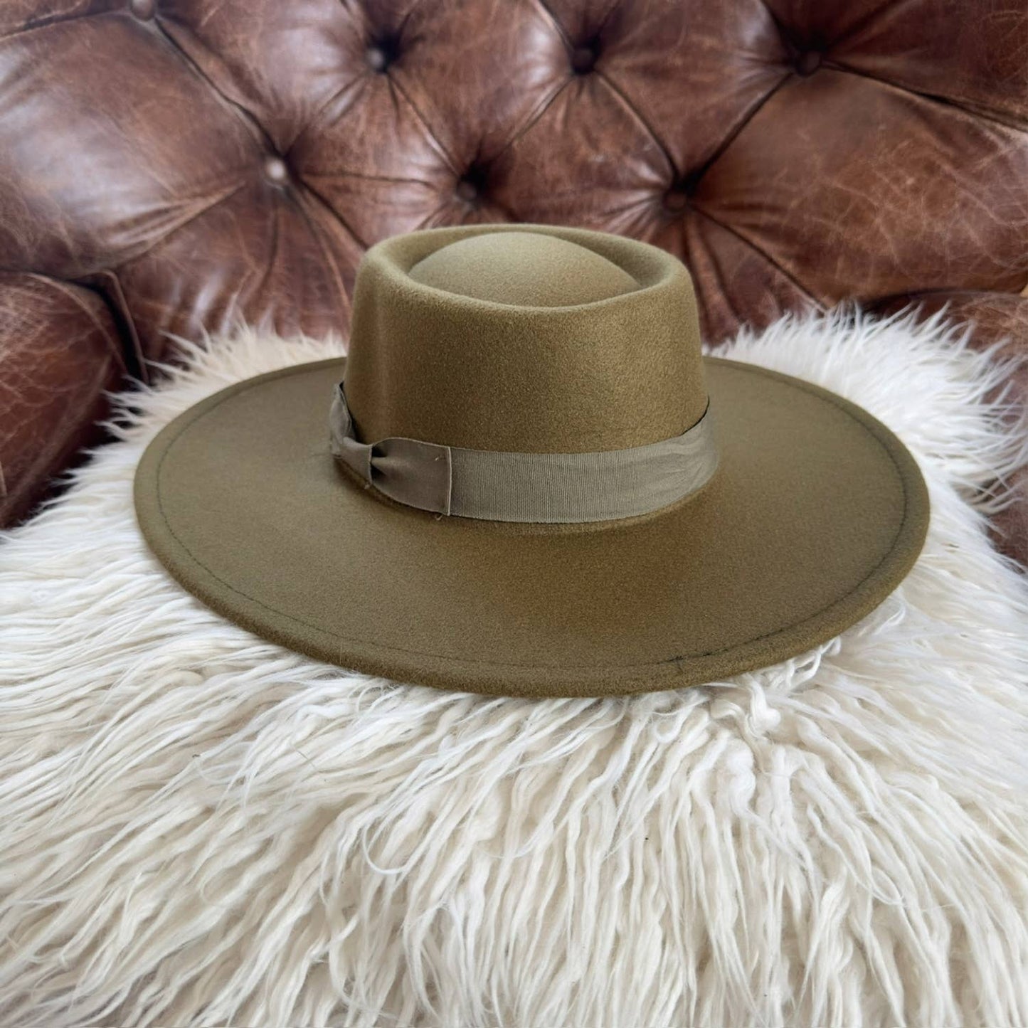 Brown fedora hat on a fluffy white surface with a brown leather couch in the background