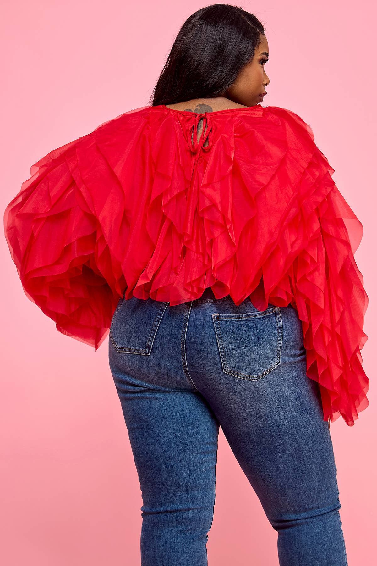 Person wearing a red ruffled top and blue jeans on a pink background