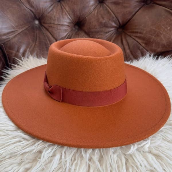 Brown hat with a red band on a white fur surface with a brown leather background