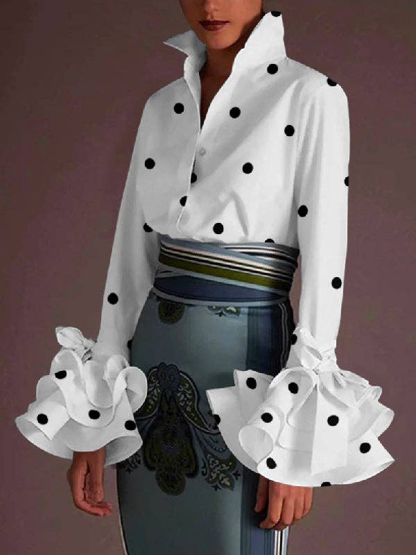 White blouse with black polka dots and ruffled sleeves on a model against a purple background