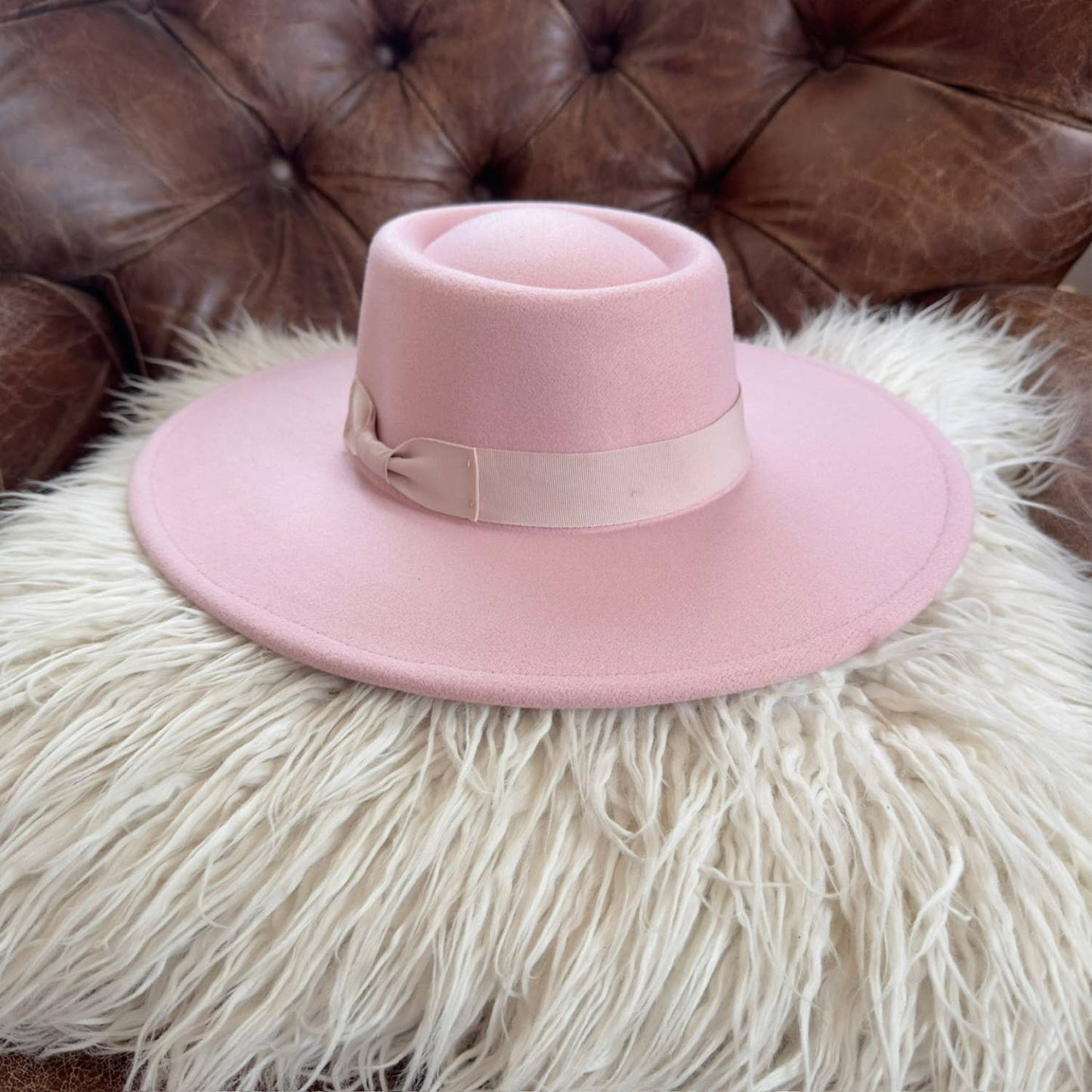 Pink hat with a ribbon on a fluffy white surface with a brown leather background
