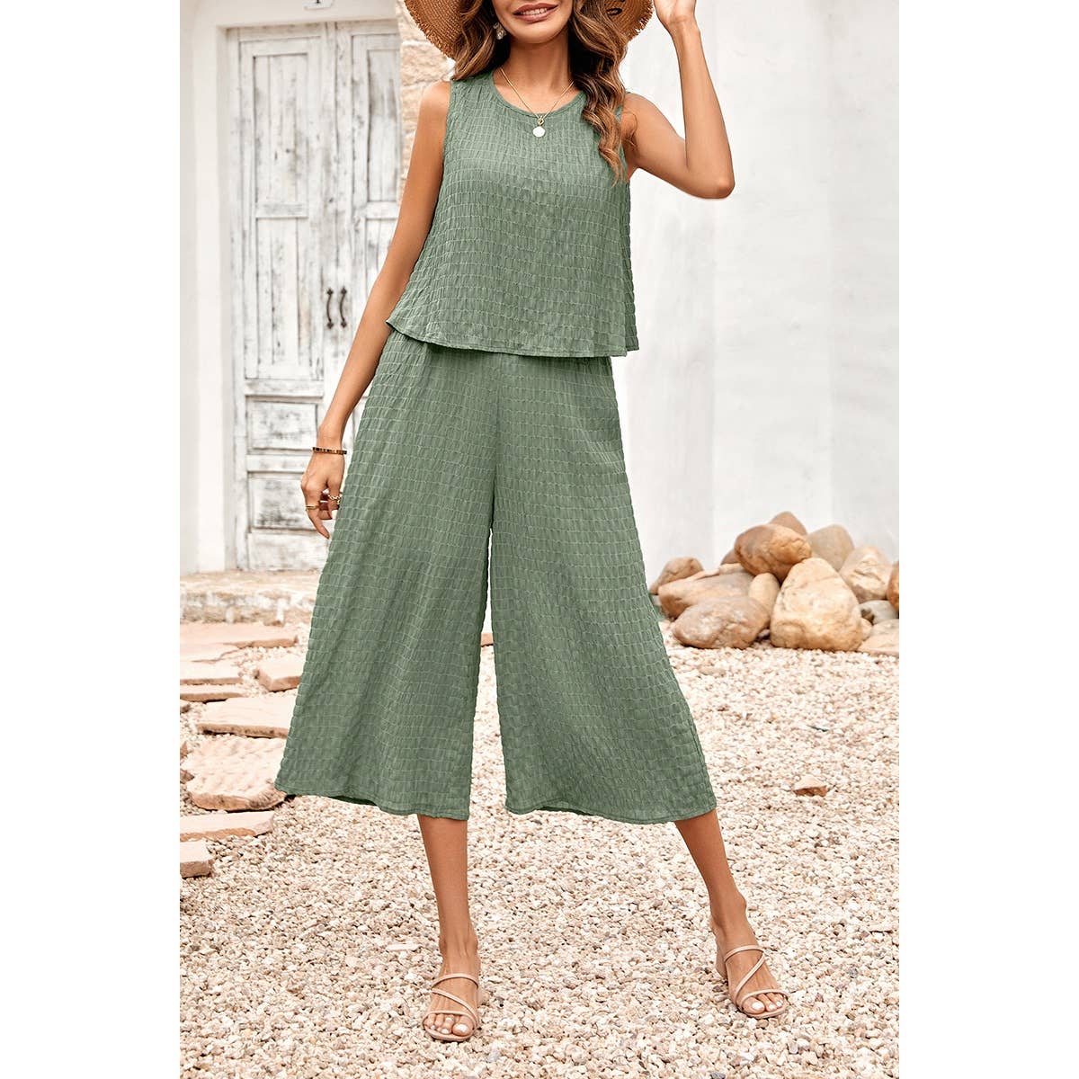 Woman wearing a green sleeveless top and wide-leg pants standing on a pebbled surface.