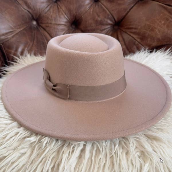 Pink hat with a brown ribbon on a fluffy white surface with a brown leather couch in the background