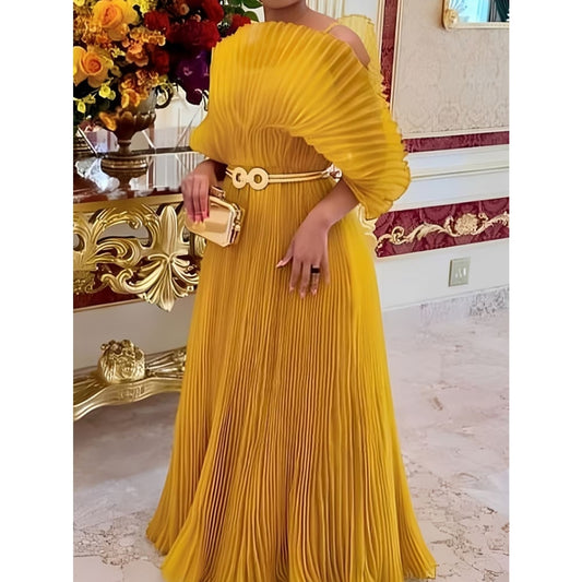 A woman wearing a pleated off-the-shoulder yellow maxi dress with a matching belt and clutch, standing in an ornate indoor setting with a gold console table and floral arrangement.