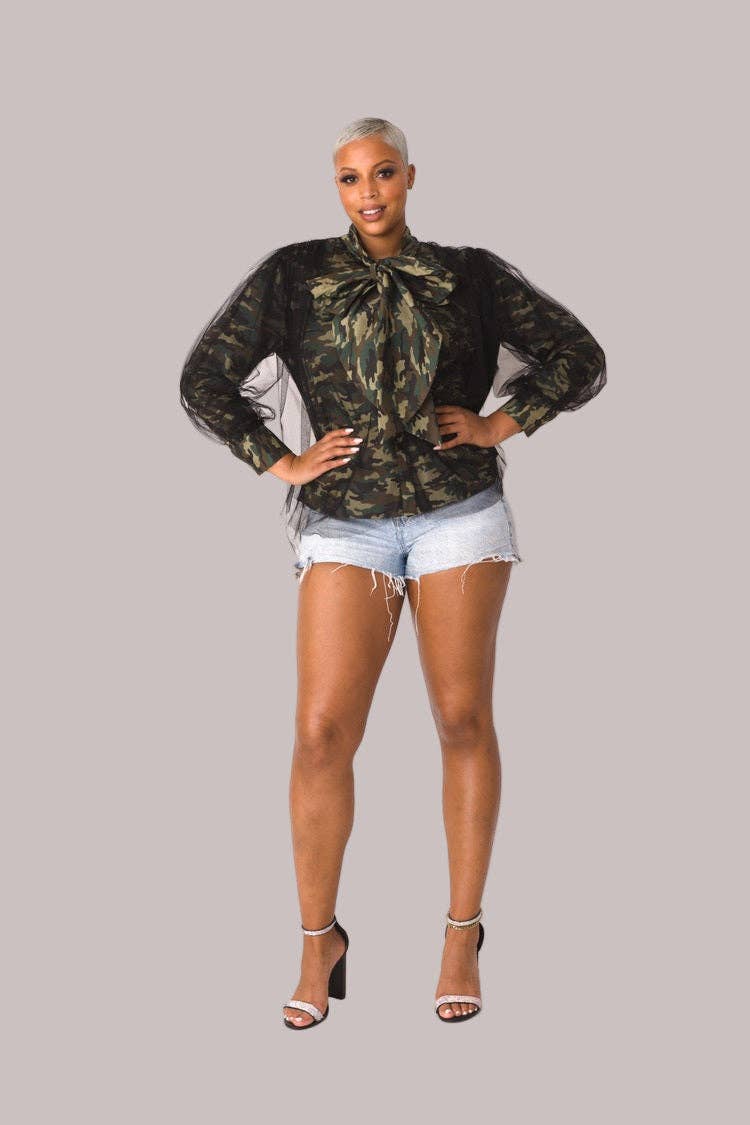 Woman wearing a camouflage top and white shorts on a gray background