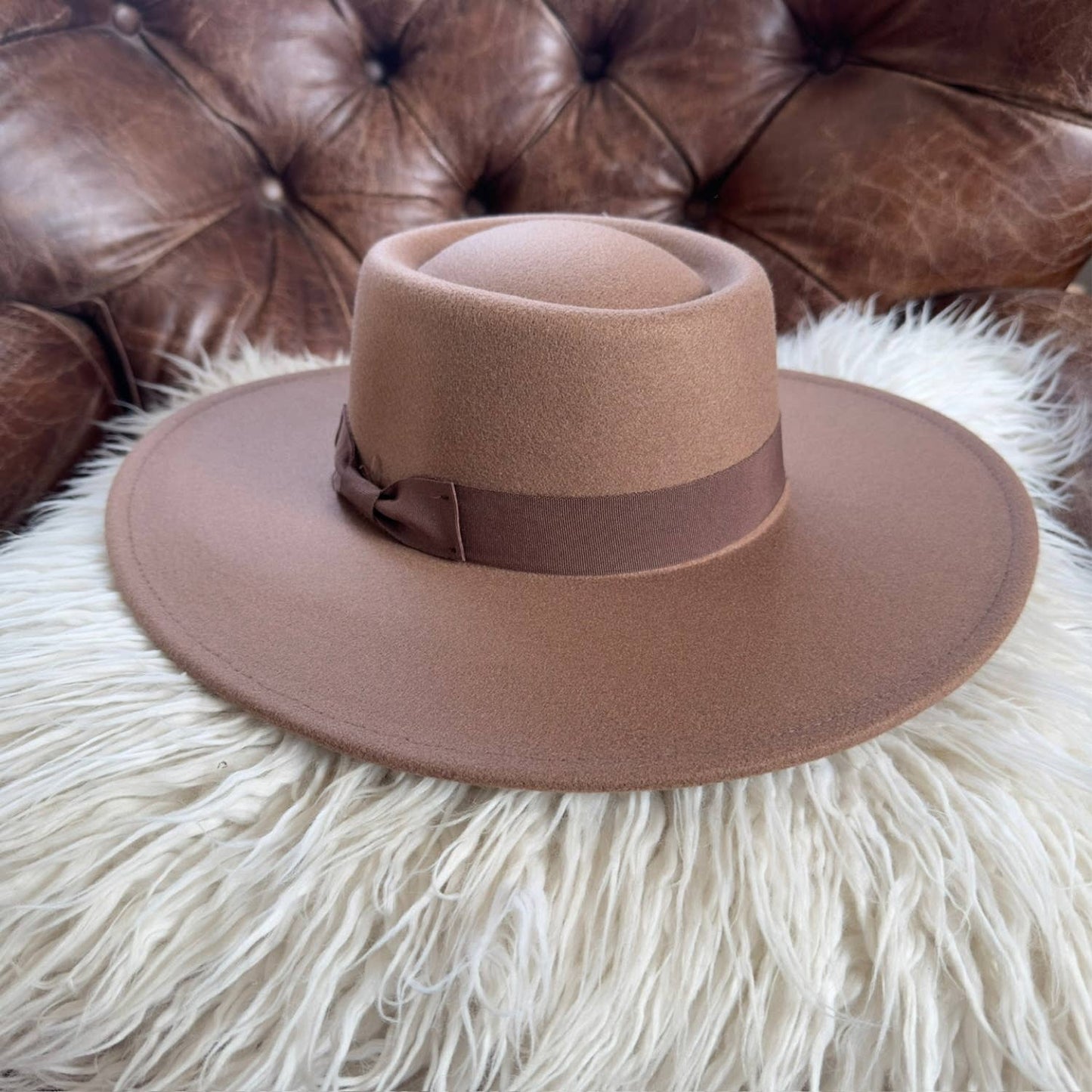 Brown fedora hat on a fluffy white surface with a brown leather couch in the background