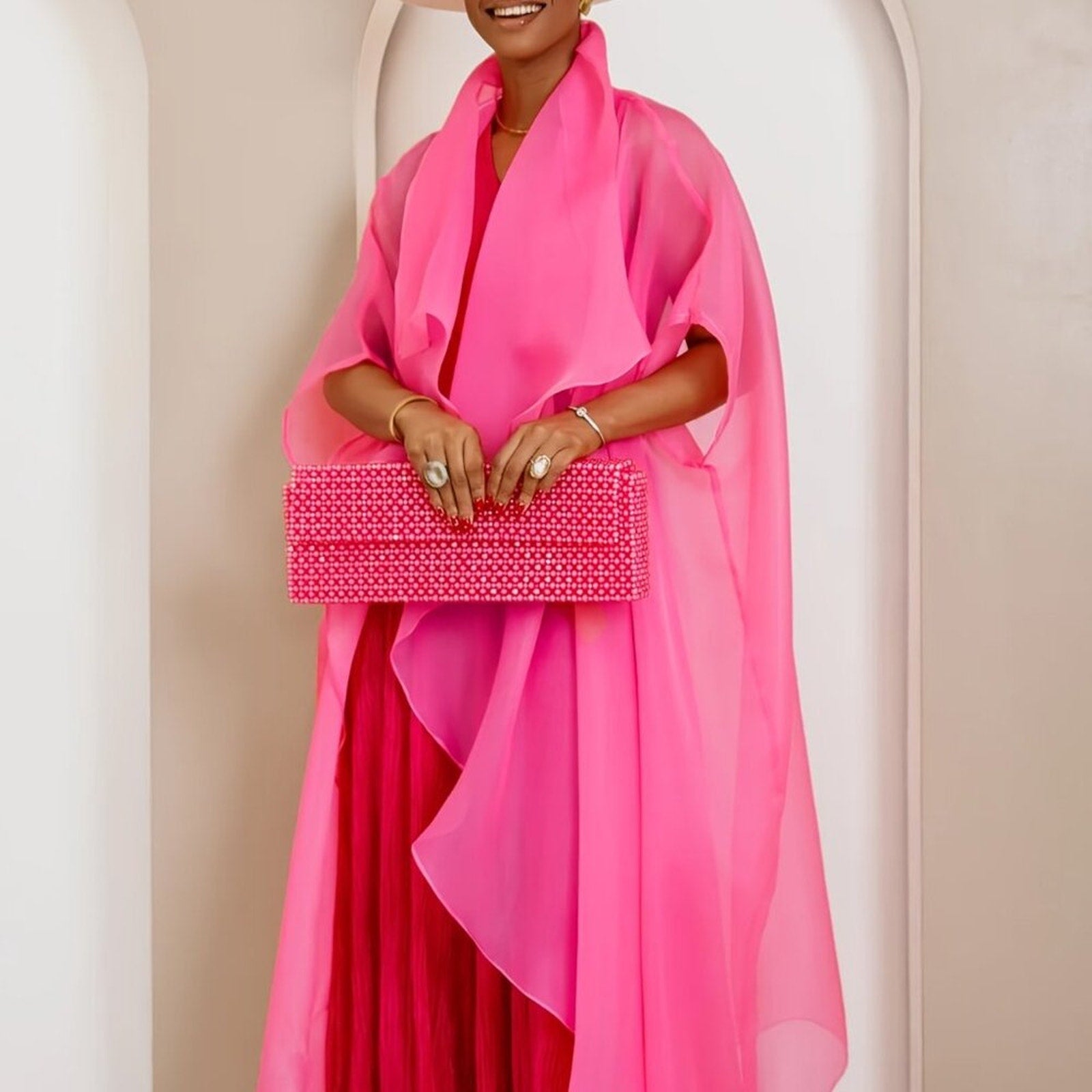 Person wearing a bright pink outfit holding a matching pink clutch against a neutral background