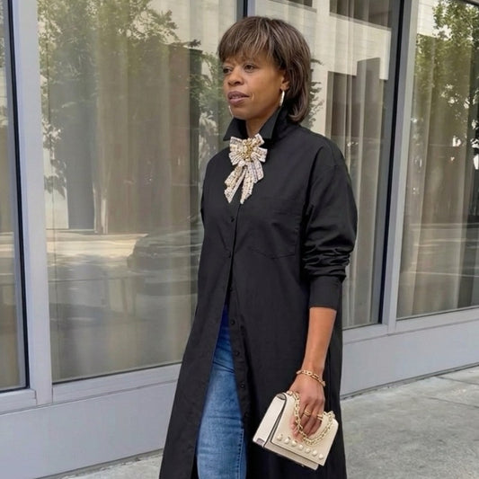 Woman wearing a black coat with a large bow and blue jeans, standing outside a building.