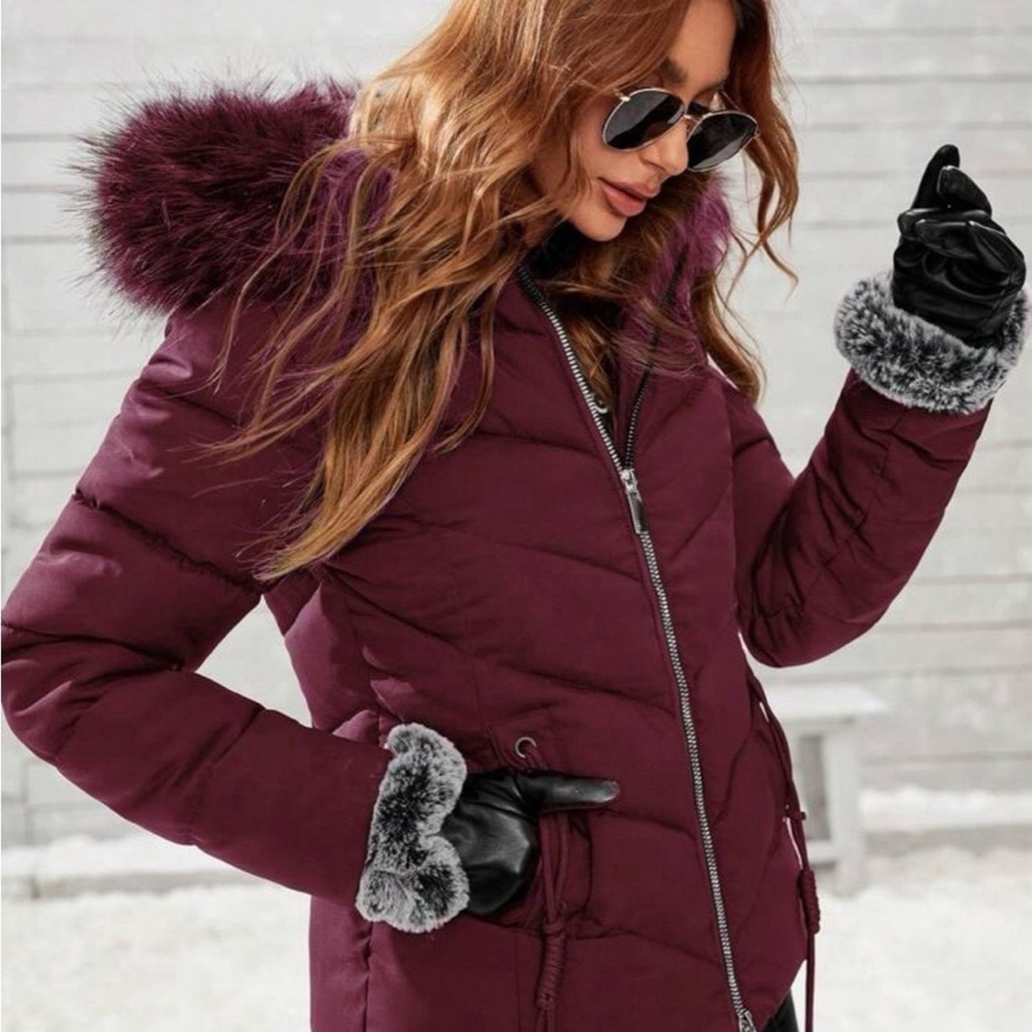 Woman wearing a purple winter coat with fur-lined hood and gloves, standing against a snowy background.