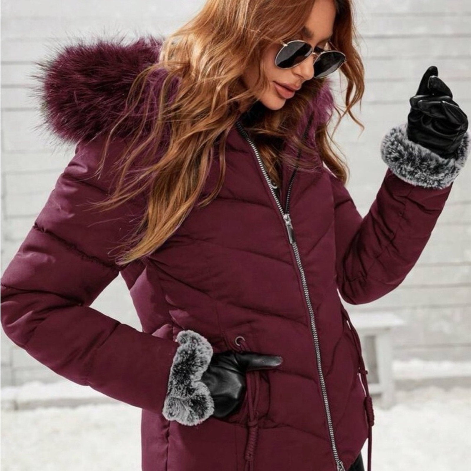 Woman wearing a purple winter coat with fur-lined hood and gloves, standing against a snowy background.