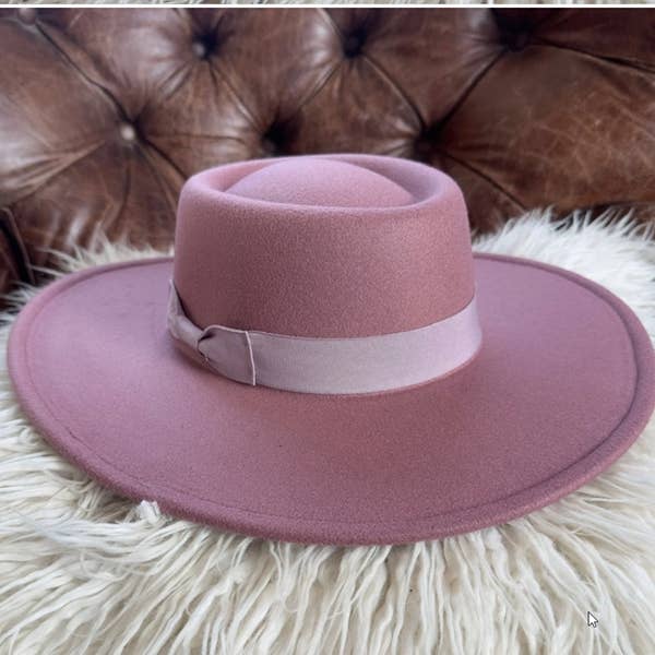 Pink fedora hat with a matching band on a fluffy white surface with a brown leather couch in the background.
