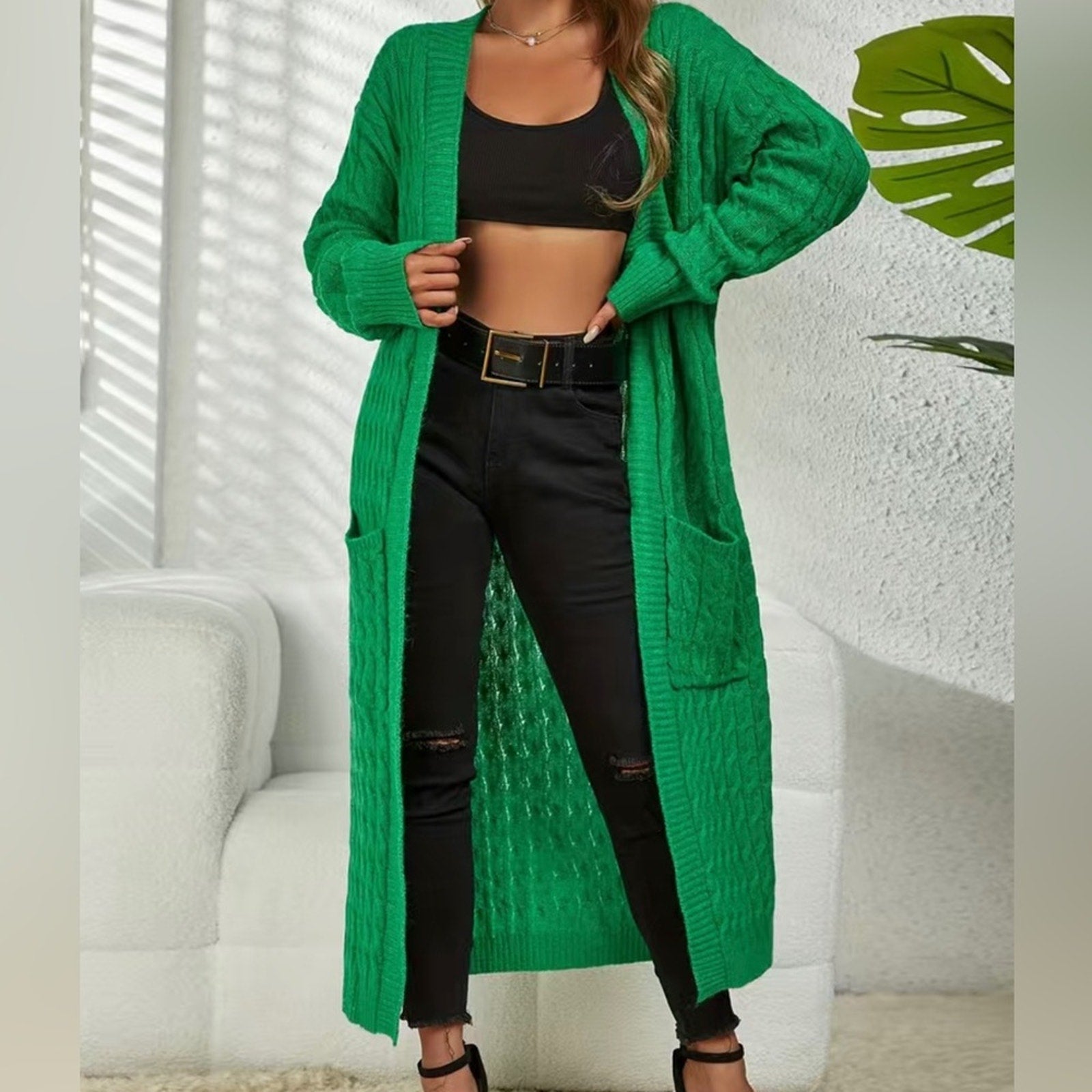 Person wearing a long green cardigan over a black outfit with a white background