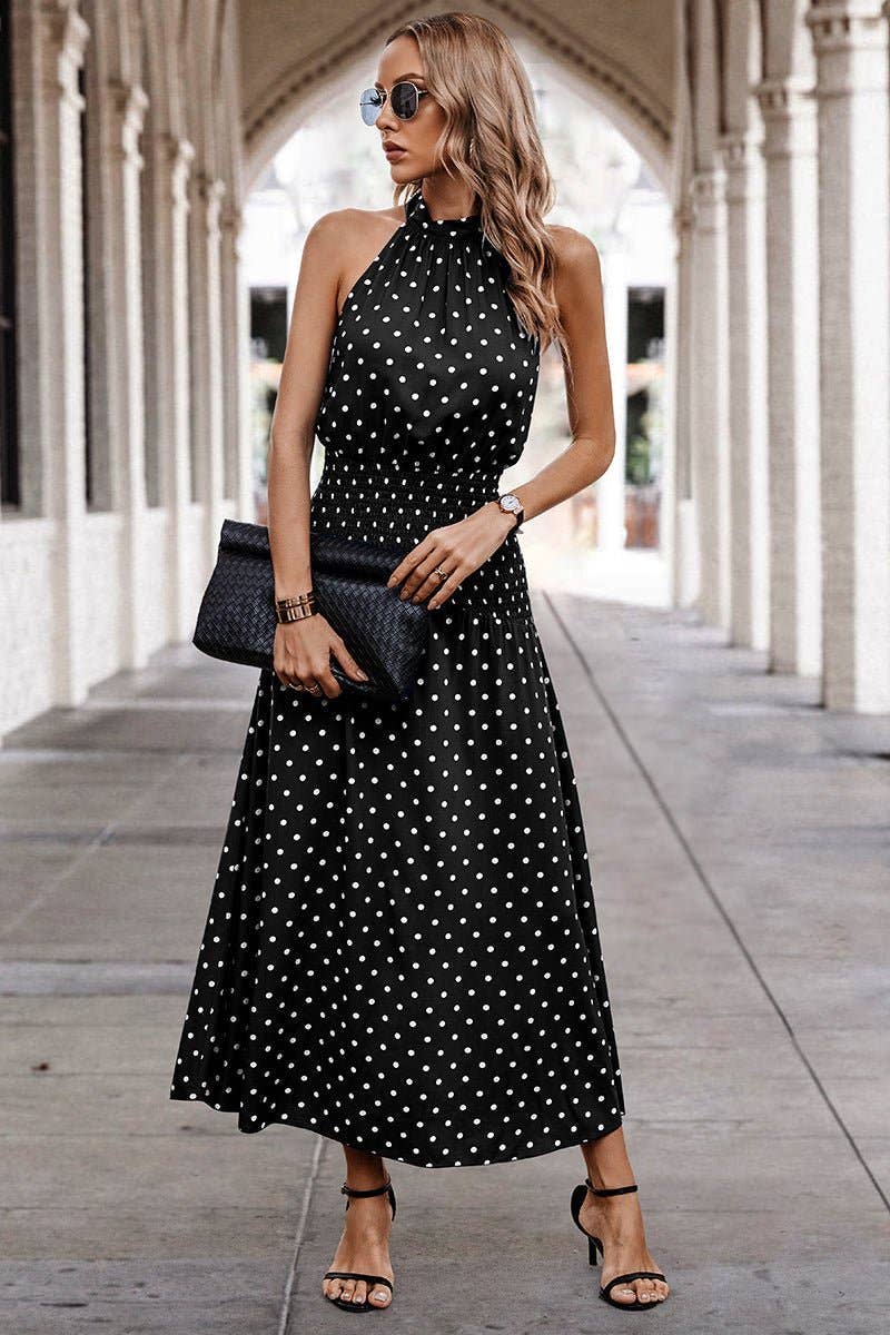 Woman wearing a black polka dot dress with sunglasses and clutch in an outdoor setting.