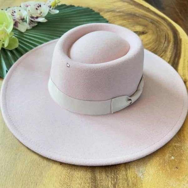 Pink wide-brimmed hat with a white band on a wooden surface.