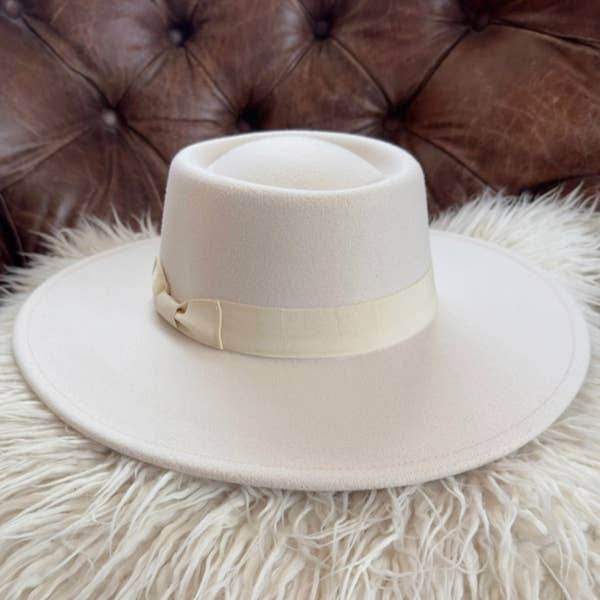 White fedora hat with a band on a fluffy white surface with a brown leather couch in the background.