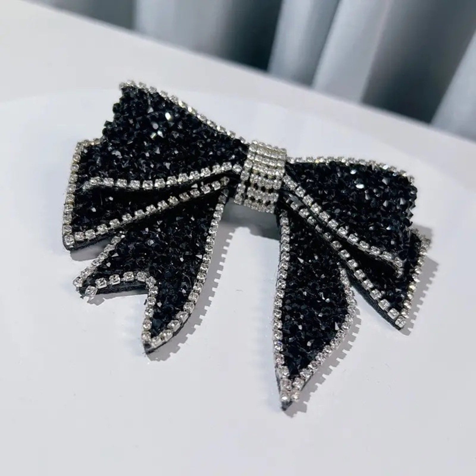 Black bow-shaped earrings with rhinestone details on a white surface.
